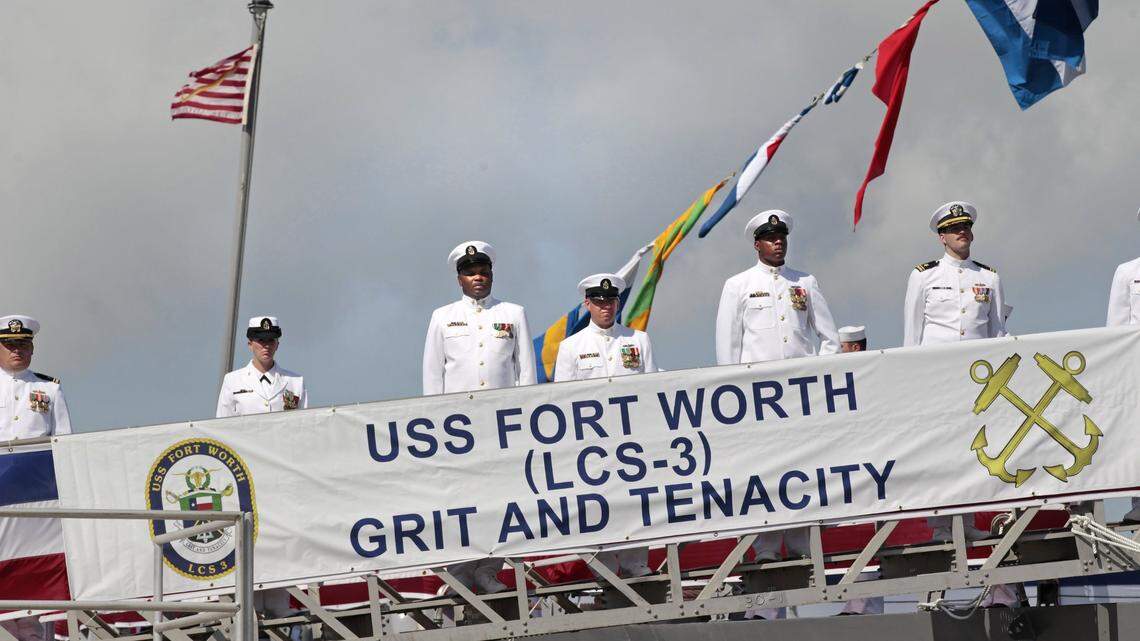 After boarding their ship, crew members stand at attention behind a banner with the ship’s motto, during the commissioning ceremony for the USS Fort Worth in Galveston, Texas, on Sept. 22, 2012.