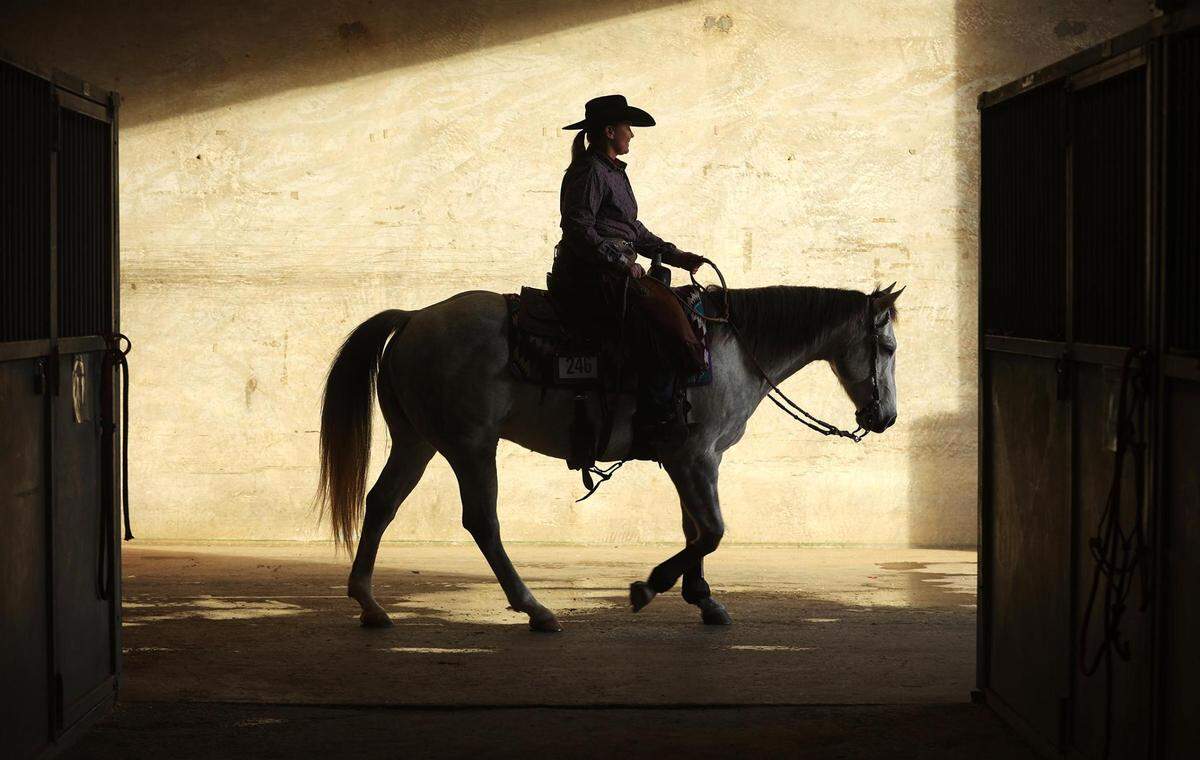Ally Hurt and quarter horse Lous Rusty Handle are silhouetted as they leave the barn during the first day of a Texas rodeo in 2021.