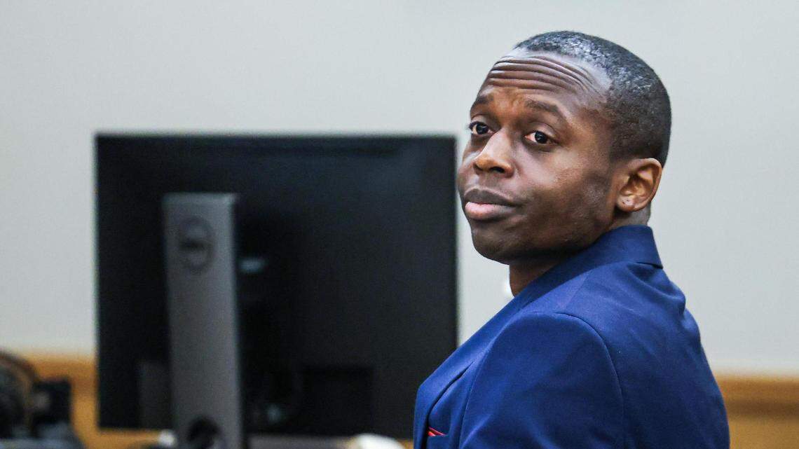 Fayaka Dunbar, in a blue suit, looks to his left while sitting down at the defense table.