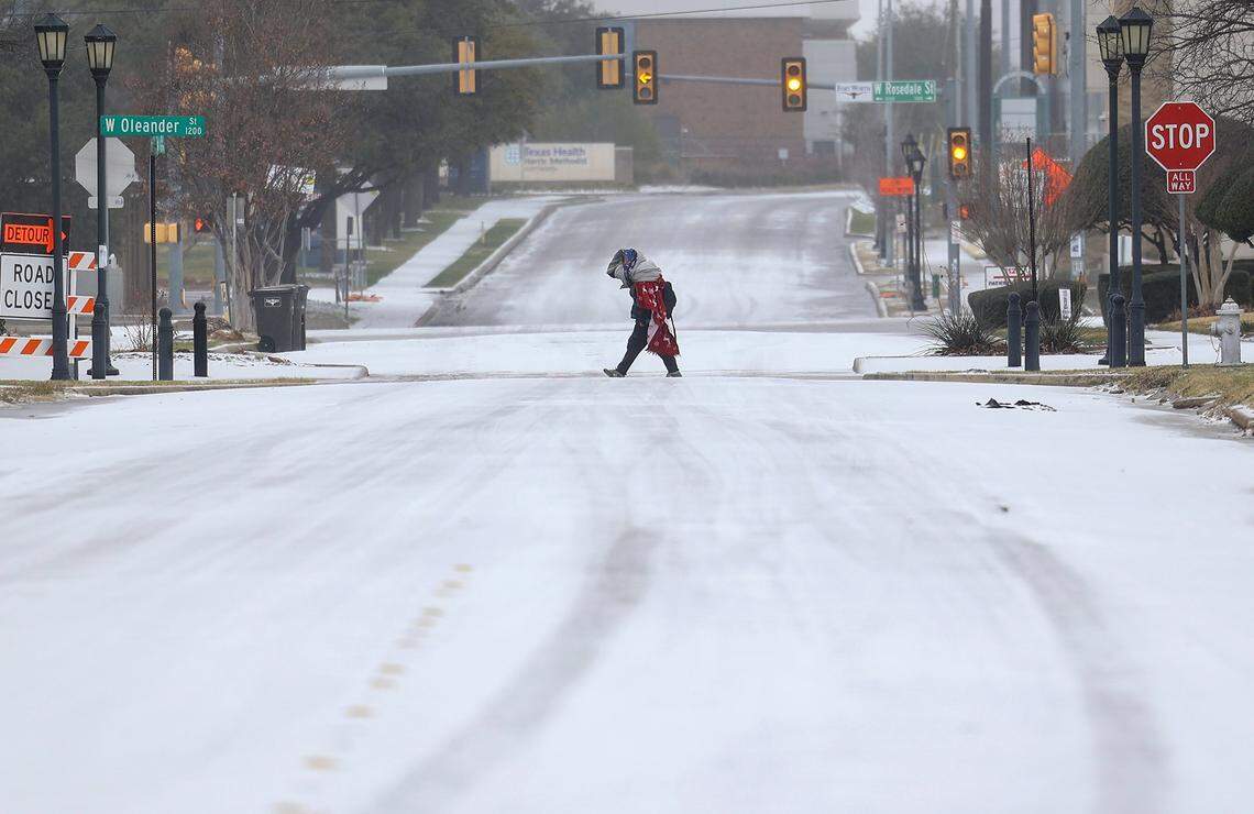A pedestrian walks along a snow West Rosedale Street on Saturday morning, Jan. 24, 2026, in Fort Worth. A massive Arctic cold front is moving across North Texas, causing freezing temperatures.