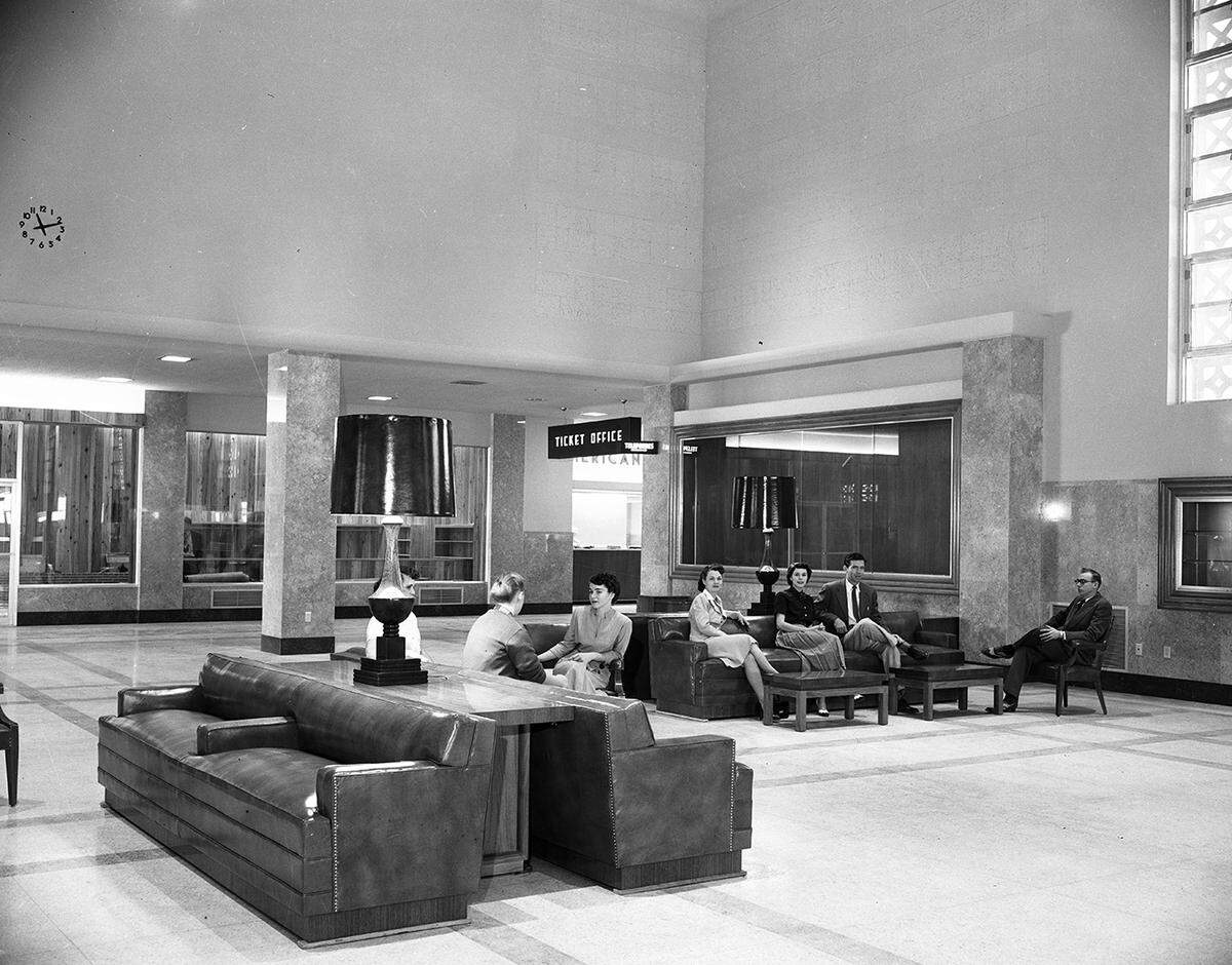Interior shot of a large room with chairs, couches, and lamps. A few people are seated.