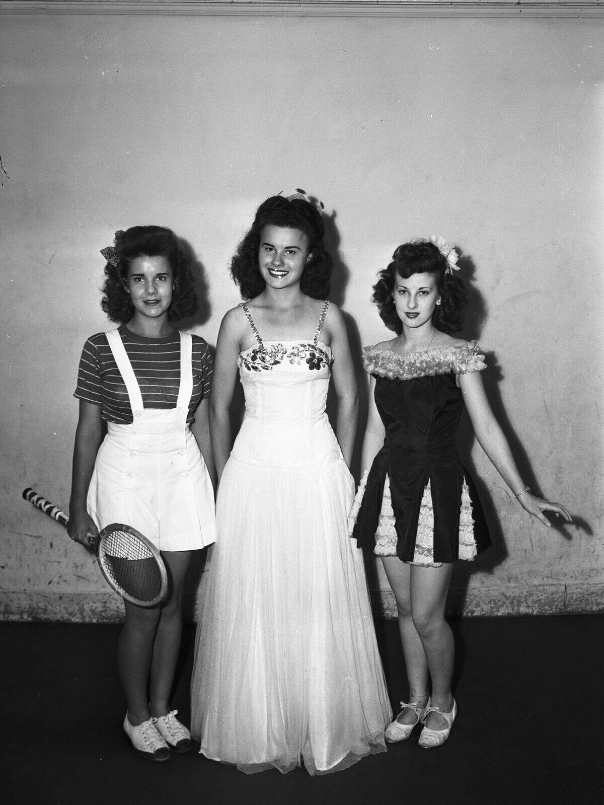 Aug. 25, 1944: Queens to be presented at the Labor Day program of the Fort Worth Recreation Department are, left to right, Virginia Echols, Jean Chandler and Bettie Armstrong. Miss Chandler is queen of sports. She is wearing a striped shirt with a jumper dress and is holding a tennis racket. Miss Chandler is queen of Labor Day. She is wearing a floor length gown and a crown. Miss Armstrong is queen of dancing. She is wearing a frilly dress, a flower in her hair, and dancing shoes.
