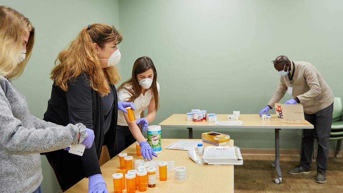 Julia Schweiger (black shirt), lab manager in Eric Lenze’s lab, organizes packets for a COVID-19 trial with the help of professional rater Leonard Imbula, and her daughters, research coordinator Abigail Schweiger (white shirt) and Nadia Schweiger (grey shirt) at the Taylor Avenue Building on April 9, 2020. MATT MILLER/WASHINGTON UNIVERSITY SCHOOL OF MEDICINE