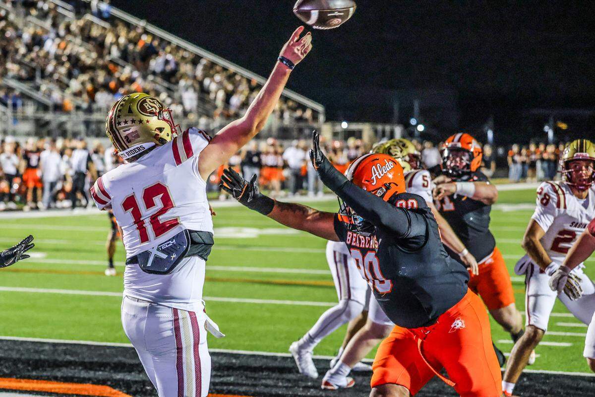 Saginaw’s Joshua Greek (12) throws a 98-yard touchdown pass despite pressure from Aledo’s Tymon Meeks (90) in a Class 5A Division I bi-district playoff game on Thursday, November 13, 2025 at Tim Buchanan Stadium in Aledo, Texas.