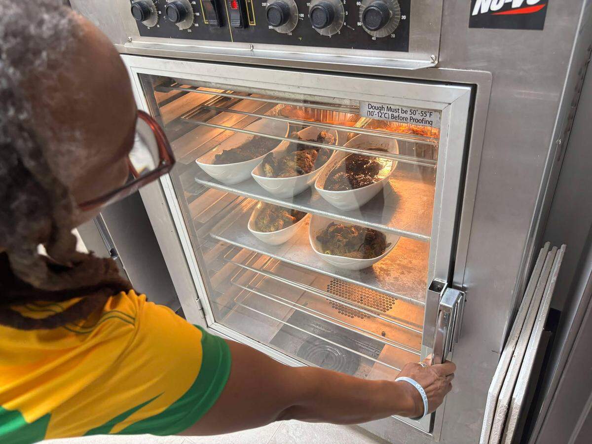Store owner Pauline Thompson checks on jerk chicken and other Jamaican dishes warming in the oven ahead of Jamrocc’s grand opening, where the meals will be served as grab and go plates
