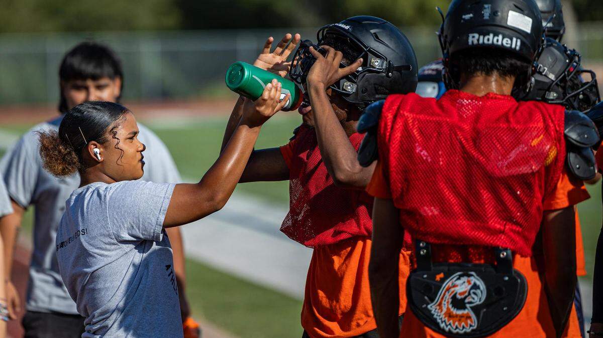 Tasia Clayton, a student in the Student Athletic Training Program, gives water to players on the Fort Worth Polytechnic High School football team during practice at the campus football field in Fort Worth on Aug. 10, 2023.