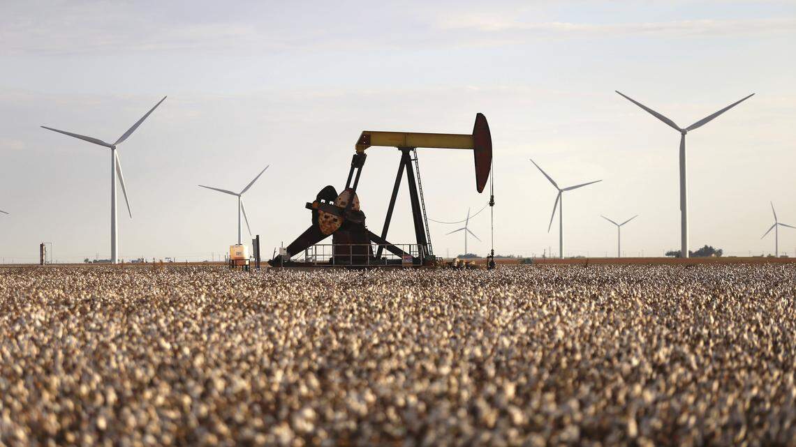 Pump jacks and wind turbines are visible inside of a cotton field near Lamesa, Texas in 2015.