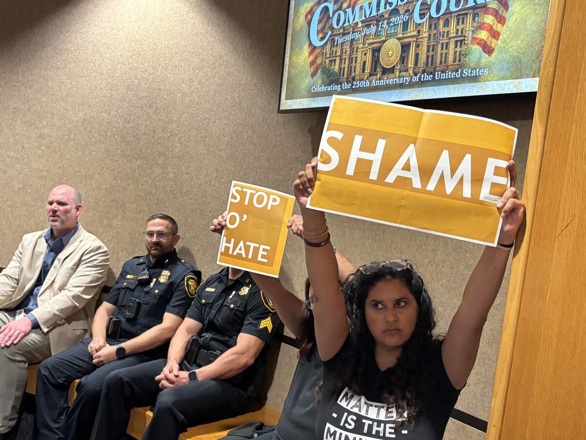 Tarrant County Commissioners Court attendees raise signs saying “shame” on July 14 while two Republicans on the commissioners court presented the Southlake Carroll school board with a recognition for their role in preventing anyone other than cisgender females from participating in female sports.