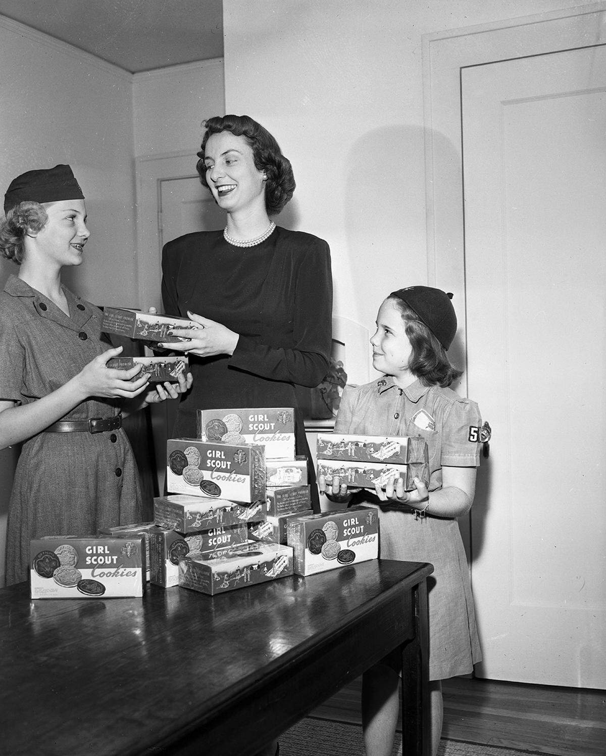 March 29, 1950: Mrs. Warren Sorrells, city-wide chairman for the annual Girl Scout cookie sale, distributes boxes of cookies to Kay Hartman, 14, left, of 1800 Hurley, a senior services Scout, and Karen Scarborough, 8, of 4221 Birchman, a Brownie.