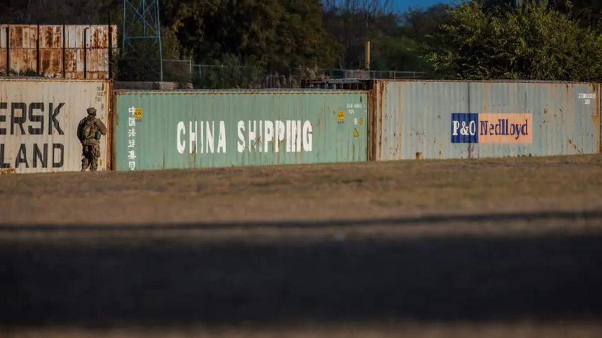 A soldier stands guard near a row of shipping containers that form a makeshift border wall along the Rio Grande in Eagle Pass.