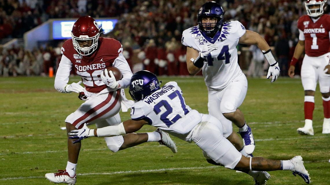 Oklahoma running back Kennedy Brooks (26) carries past TCU safety Ar’Darius Washington (27) and defensive end Colt Ellison in the first half of an NCAA college football game in Norman, Oklahoma, Saturday, Nov. 23, 2019.