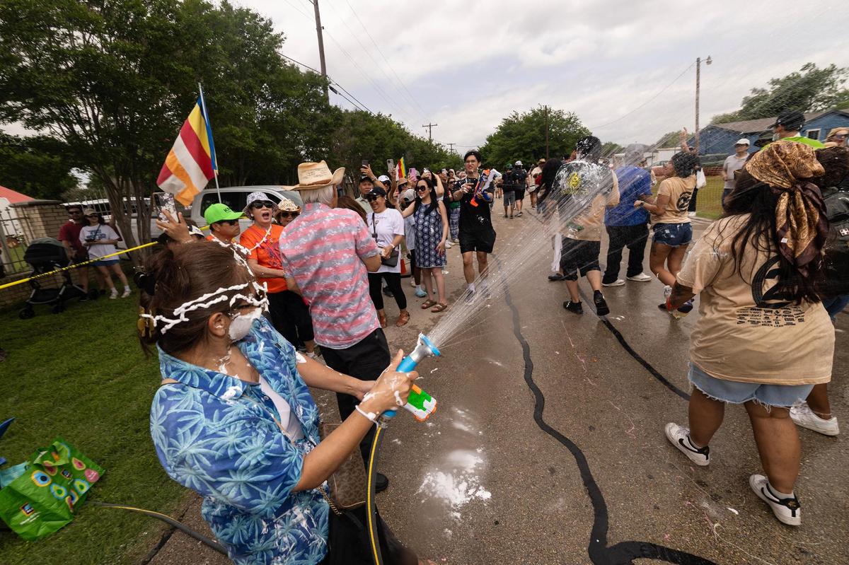 A festival attendee uses a hose to spray water on the parade walkers during the Lao New Year parade on the third day of the Lao New Year festival at Wat Lao Thepnimith Temple in Saginaw on Sunday, April 27, 2025.