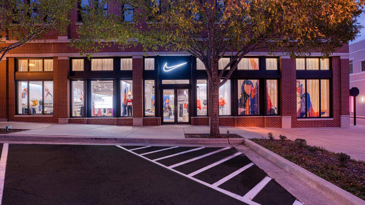 A Nike Live location shows a blue neon Nike swoosh logo, mannequins modeling orange and red athletic apparel and window art in the display.