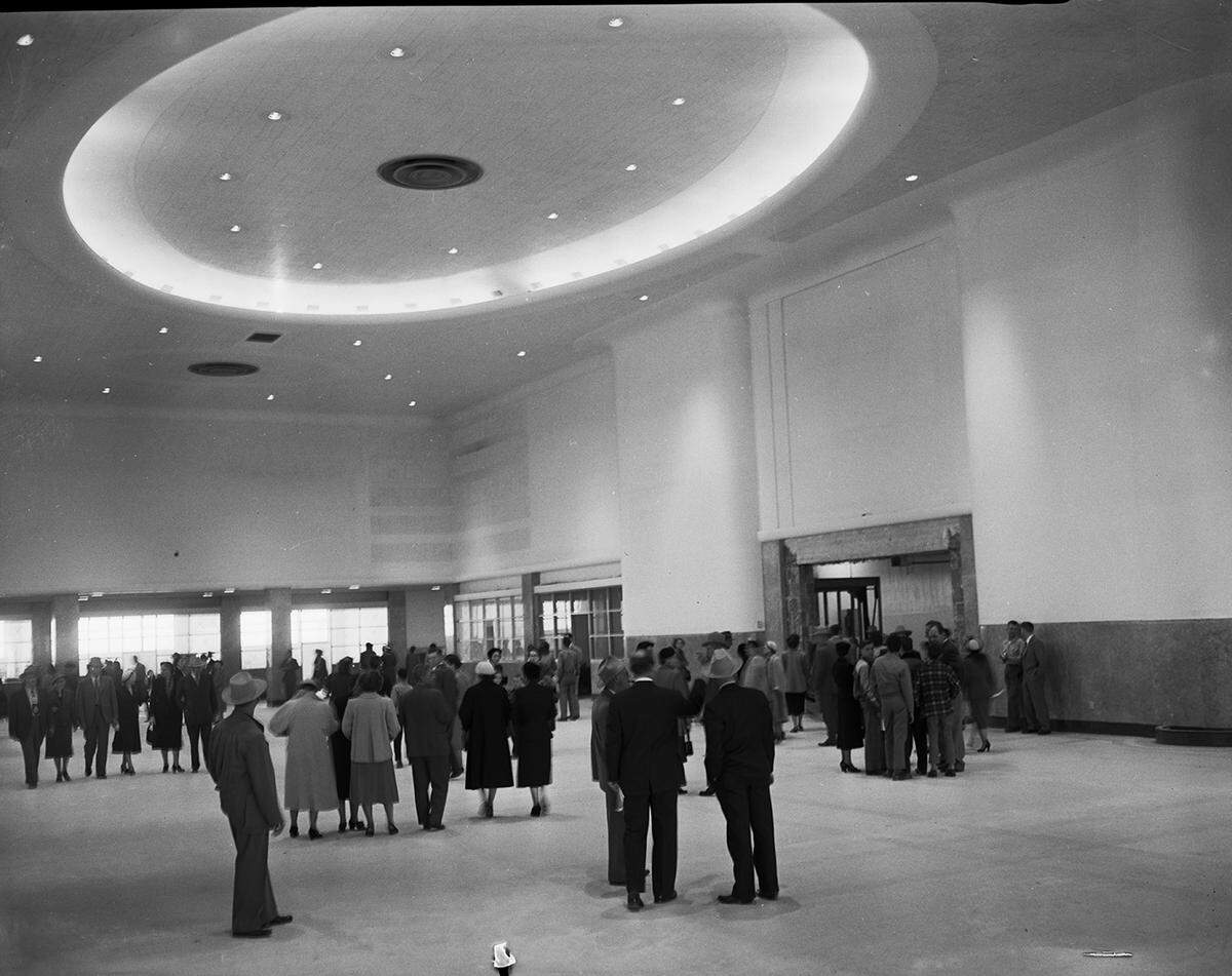 Well-dressed visitors look around the high-ceiling terminal, which features a large circular light.