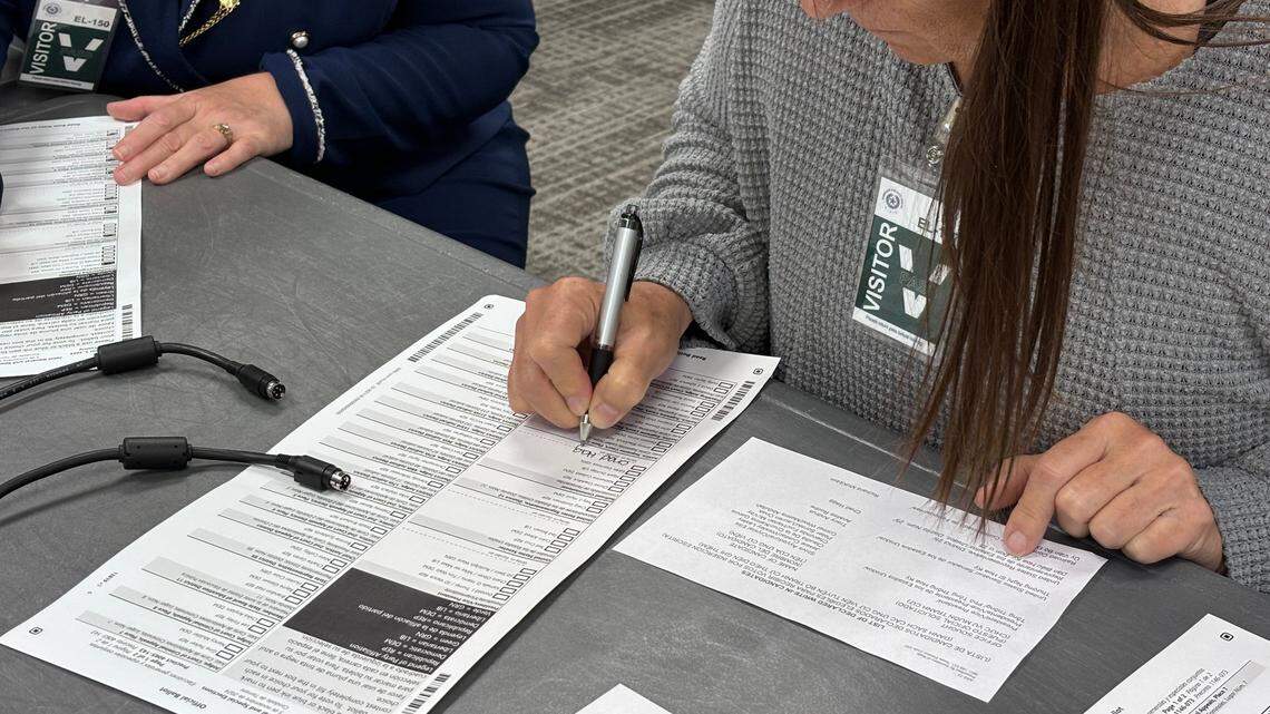 Tarrant County resident Janet Jones fills out a mock mail-in ballot at the public test of the county’s elections on Sept. 16, 2024. A woman in a grey sweater fills out a form while seated at a table. She is wearing a name tag that says "Visitor" on it.