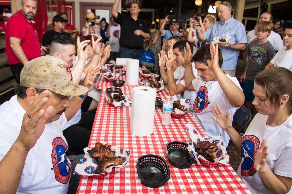 Competitors raise their hands at the 17th annual rib eating competition at Riscky’s Barbeque in the Fort Worth Stockyards in 2023.