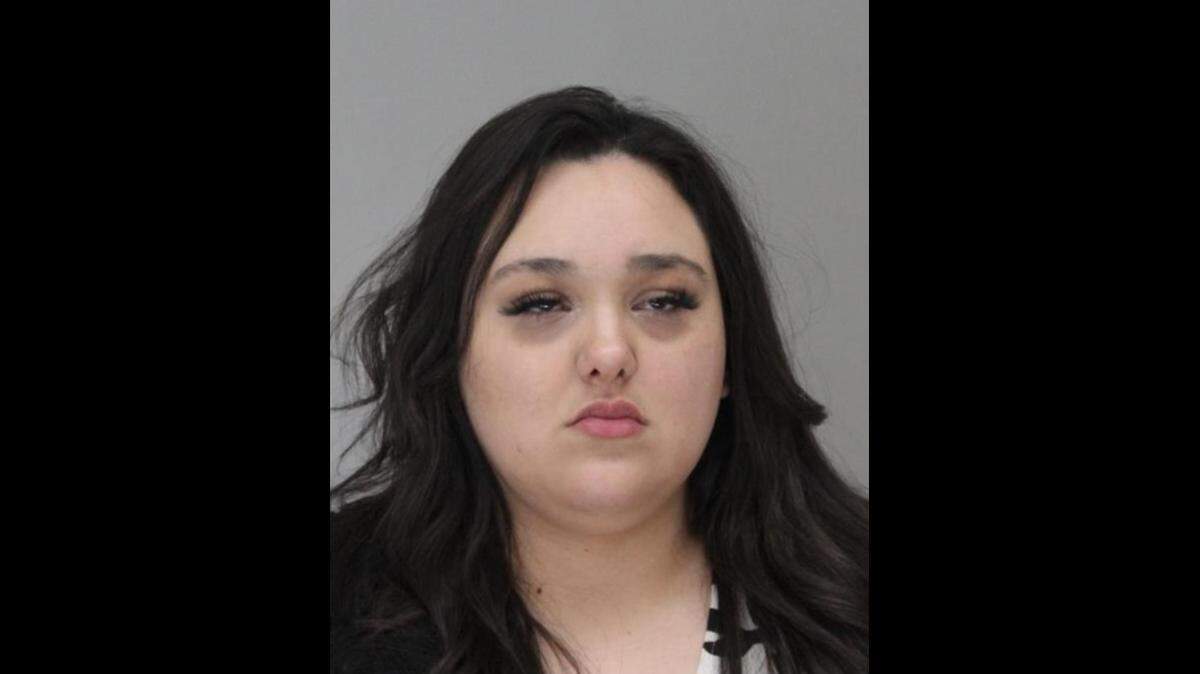 A mugshot of a woman with straight black hair and porcelain skin with a portly physique.