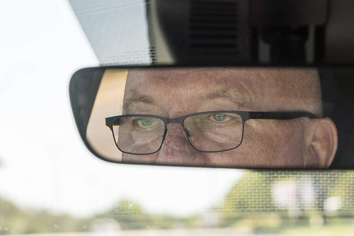 An older man’s eyes can be seen framed in the rearview mirror of a vehicle.
