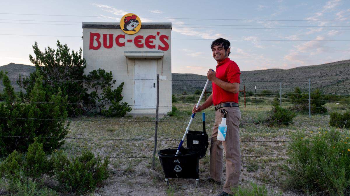 A small, stand alone building with the Buc-ee's beaver logo and name on the outside with a Buc-ee's worker in front prepared with a mop and bucket.
