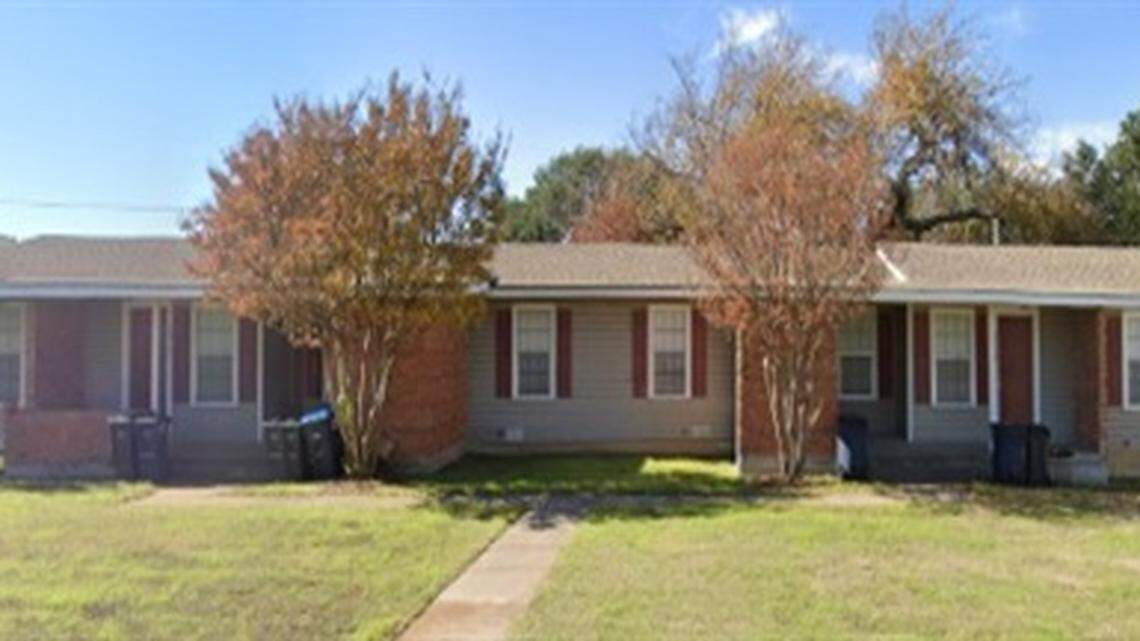 A one story ranch style home with two brown-ish tree/bushes in front