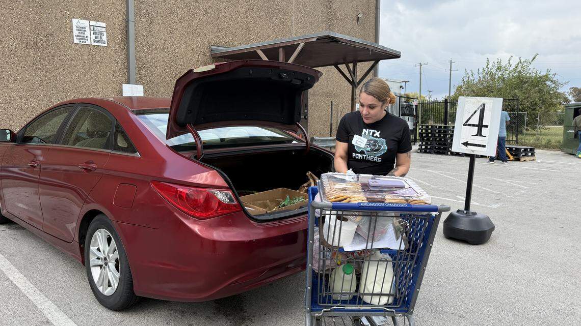 Melissa Salinas, an Arlington Charities volunteer, loads a vehicle with groceries as more neighbors in cars line up to have their orders fulfilled.