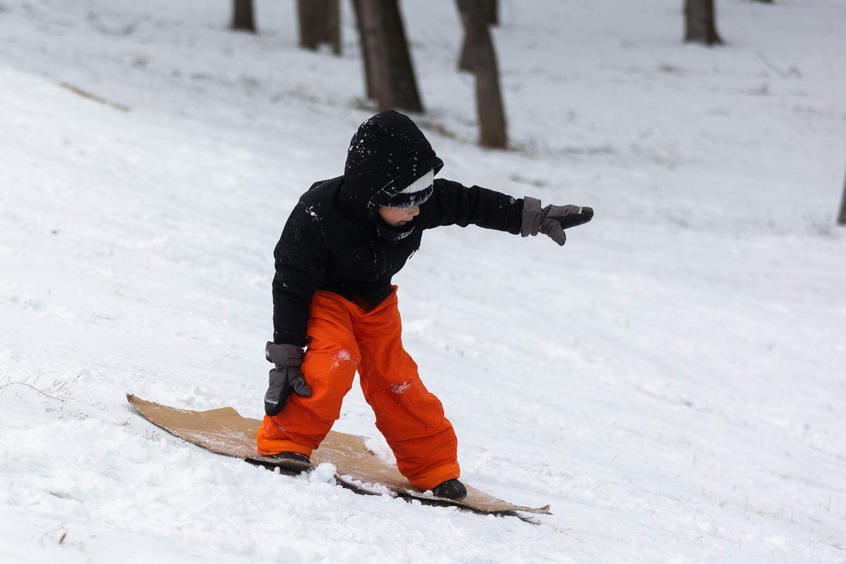 Kayden Taylor, 9, stands up on a piece of cardboard he is using to sled down the hill Thursday, Feb. 3, 2022, in Fort Worth.