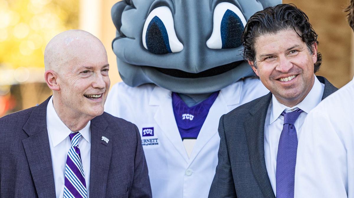 Two men and a frog mascot standing a smiling
