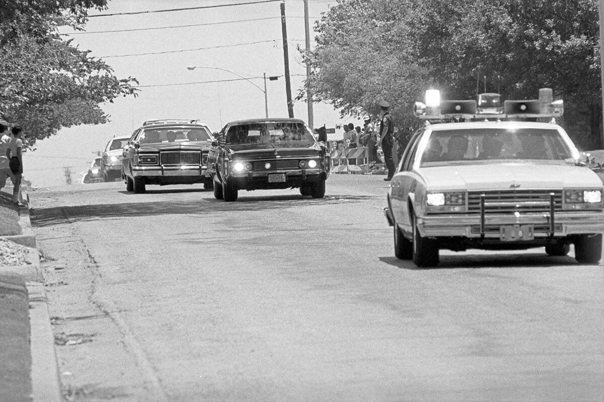 Carter's limo is between two police cars driving down a street.