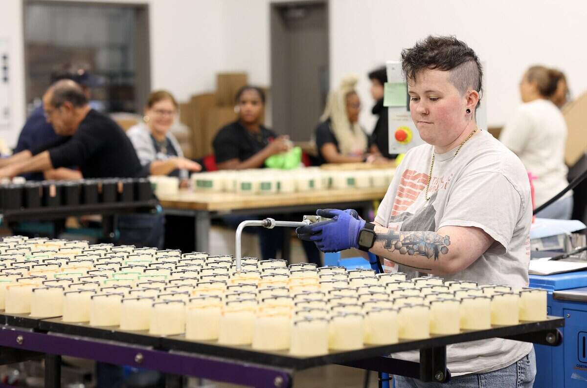 Yoshi Hughes, an apprentice machine operator, fills glass containers with hot wax while making candles at Calyan Candles on Friday, Sept. 12, 2025, in Arlington.