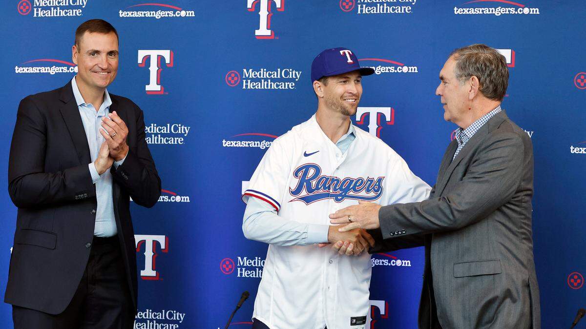 Texas Rangers starting pitcher Jacob deGrom, center, shakes hands with new manger Bruce Bochy after trying on his new jersey during a press conference at Globe Life Field in Arlington, Texas, Thursday, Dec. 8, 2022. General Manager Chris Young, left, introduced the star pitcher who signed a five-year contract until the year 2027. (Tom Fox/The Dallas Morning News via AP)