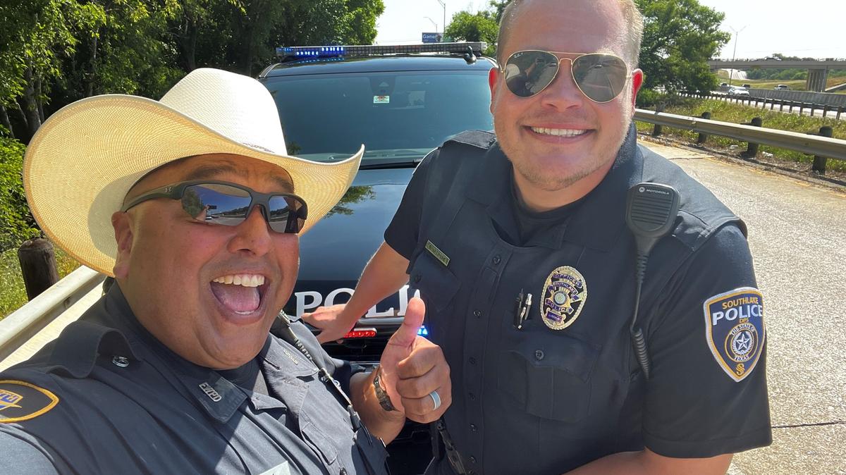 A smiling police officer in a cowboy hat poses for a picture with a smiling officer in mirrored sunglasses.