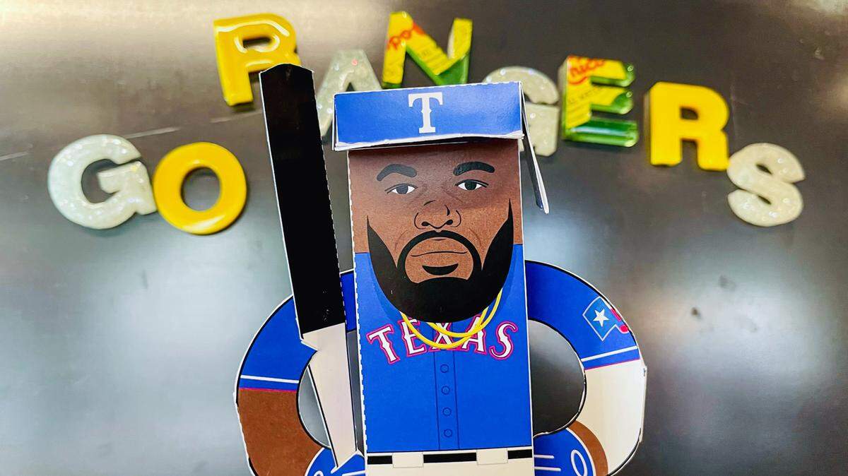 Paper cutout figure of Adolis Garcia in his blue ranger uniform and a cutout bat on his shoulder.