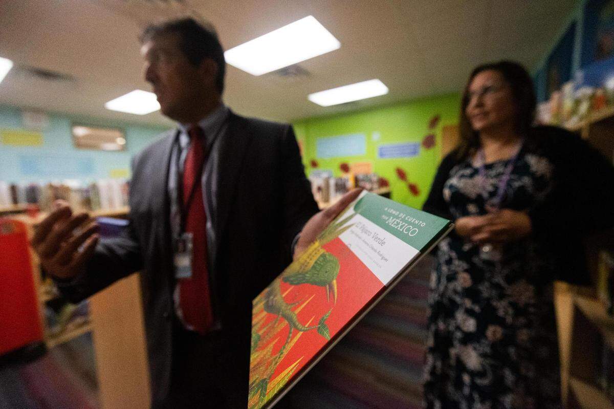 Principal Ricardo Alvarez Uzcategui holds up a Spanish-language book at the library on Nov. 9, 2022, at M.H. Moore Elementary School in Fort Worth. A new funding model allowed the school to purchase more books for its library.