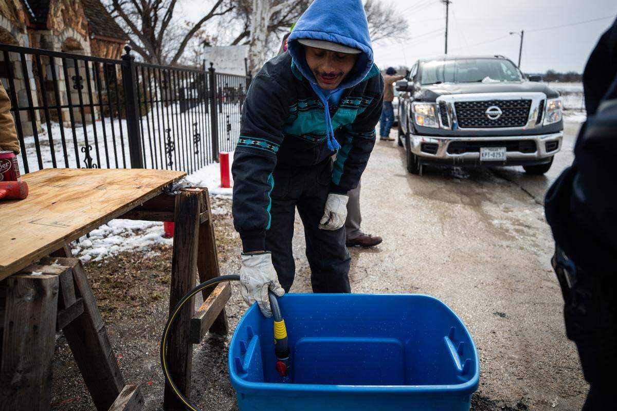 Daylen Powell fills a plastic tote with spring water from Burger’s Lake on Thursday.. The spring flows to the Trinity River in the winter and was diverted to help people without water.