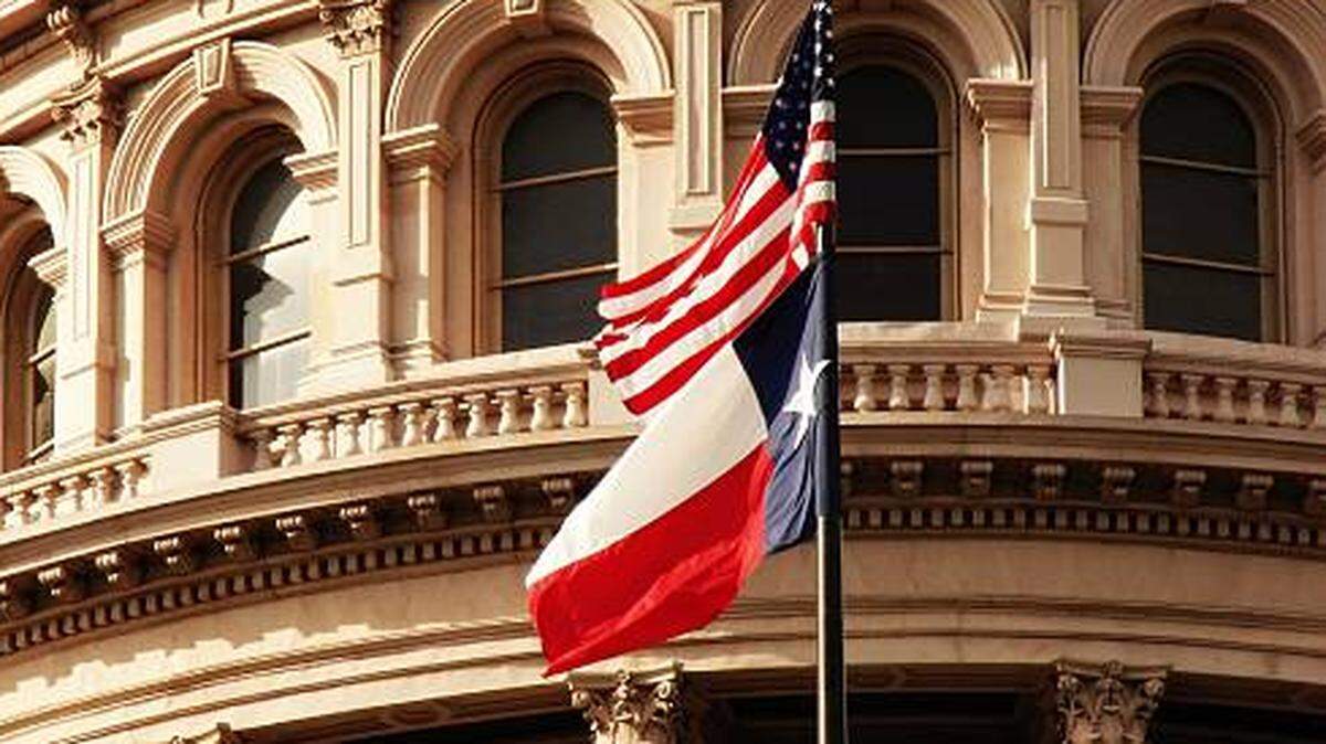The American and Texas flags wave in front of the Texas State Capitol in Austin.
