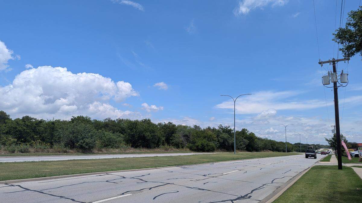 A long look down a road with trees on the left and cars passing by
