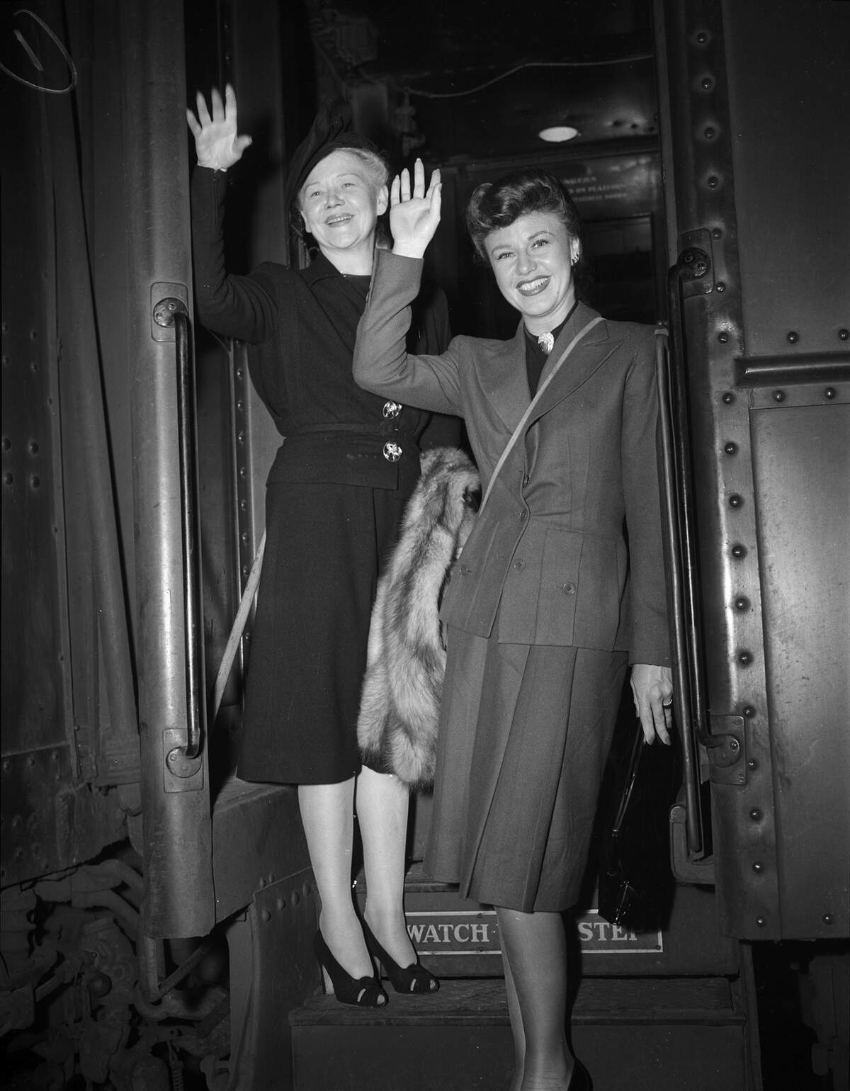 Miss Rogers is wearing a blazer with a pleated skirt. Mrs. Rogers is wearing a hat, blouse, skirt, and is carrying a fur shawl.