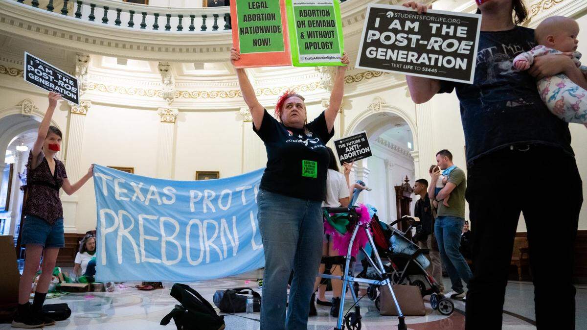 Betsy Riot, center, holds her signs above her head while protesting at an International Women’s Day Sit-In for Abortion Rights in the Texas State Capitol Rotunda, March 8, 2023. Both abortion rights and anti-abortion protesters were present on the rotunda, speaking to curious passers-by, singing songs and occasionally chanting. International Womens Day Sit In Austin Texas Sed 01