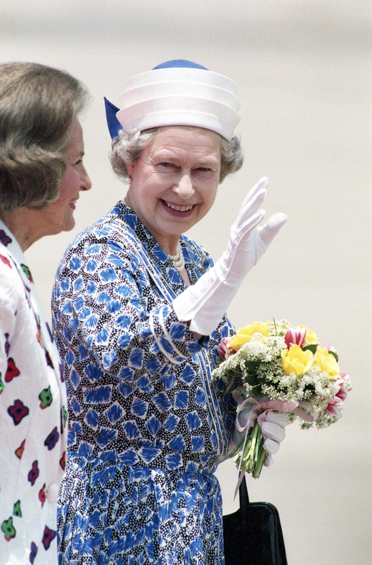 Queen Elizabeth II waves to a crowd of people upon her arrival at Love Field in Dallas with Dallas Mayor Annette Straus on her right.