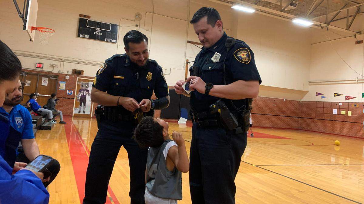 Fort Worth police officers give badge stickers to an eager after school basketball player.