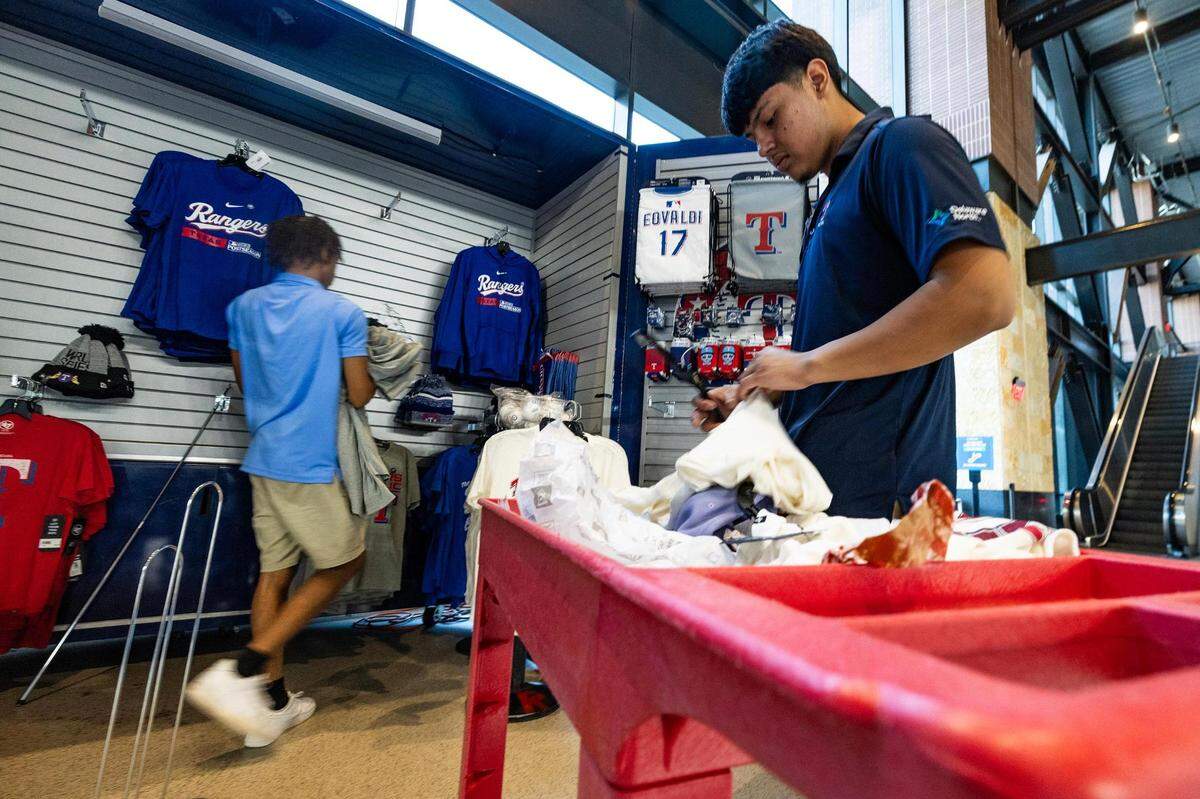 Retail supervisor Jayden Carter and Andrew Rosales stack shirts at a merchandise kiosk during 2023 World Series Media Day at Globe Life Field in Arlington on Thursday.