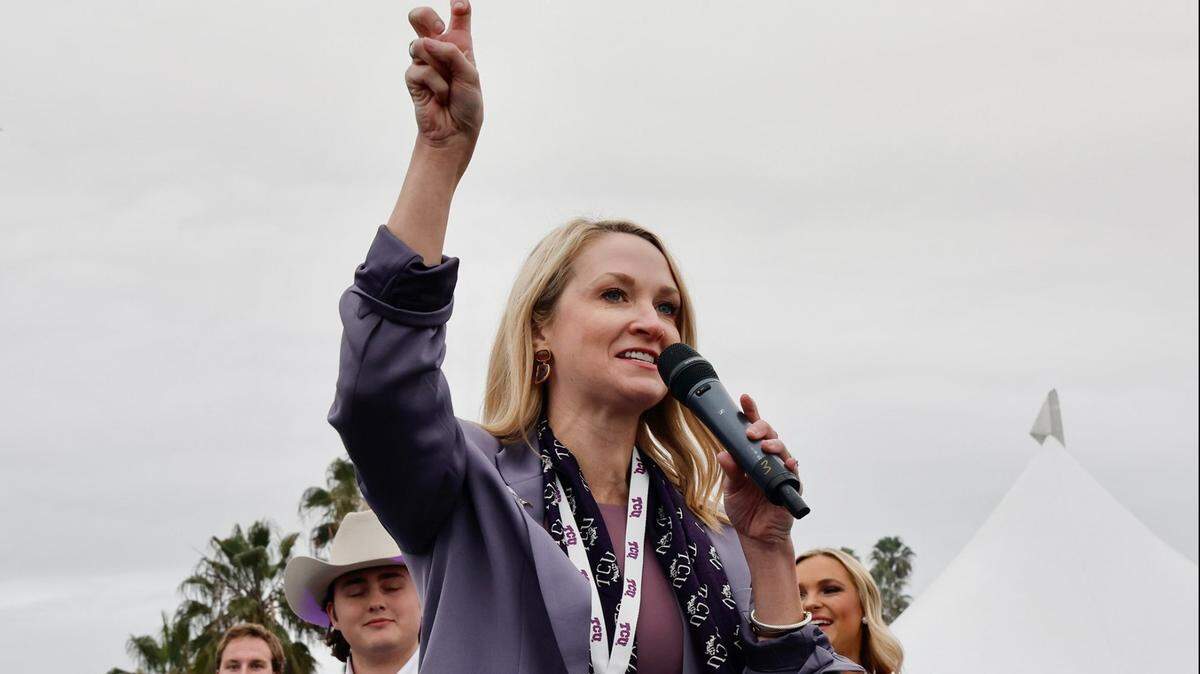 Fort Worth Mayor Mattie Parker holding a microphone in her left hand and making a "go frogs" TCU hand gestures with her right hand. 