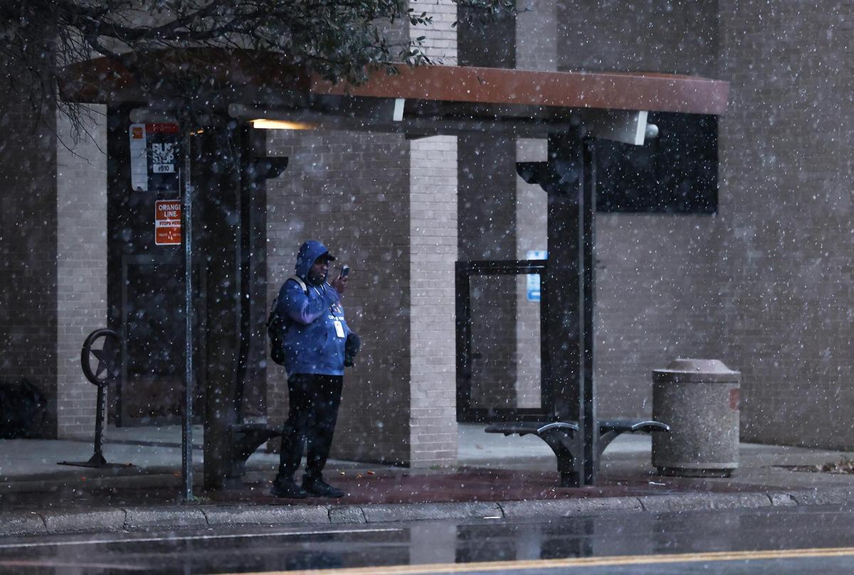 Snow falls as Chris Hall waits at a bus stop on Houston Street in downtown Fort Worth to go home after a night shift on Thursday, Jan. 9, 2025. A winter storm warning is in effect for North Texas.