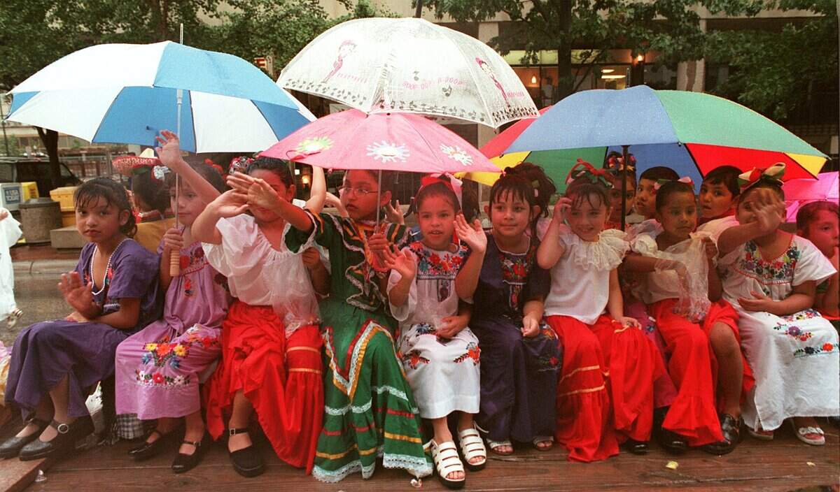Sept. 12, 1998: Children from Diamond Hill Elementary seek shelter from the rain while riding on the Ballet Folklorico float during the El Dieciseis de Septiembre parade in downtown Fort Worth. The parade was sponsored by the Mexican Independence Day Parade Committee.