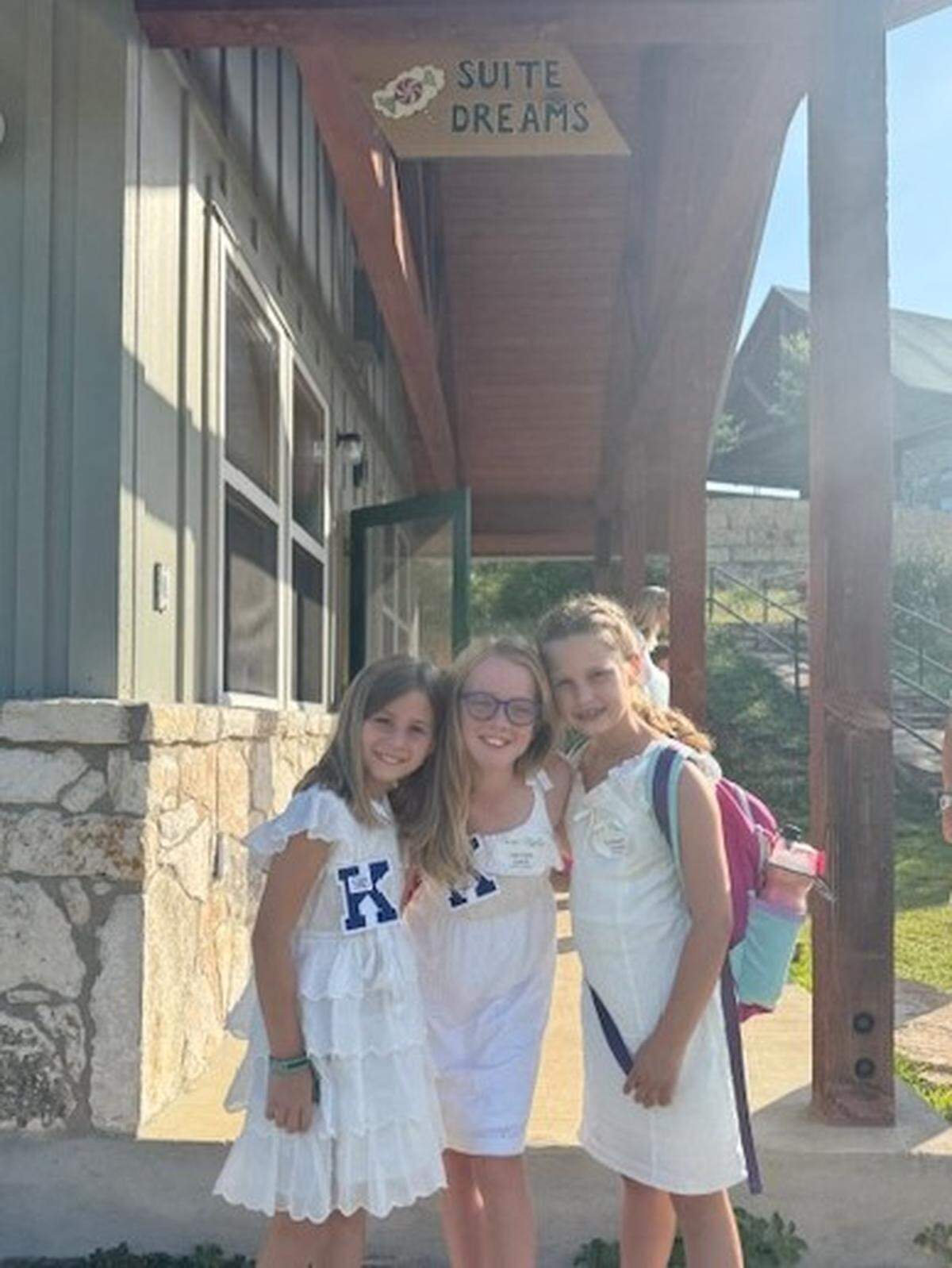 Binney Gilpin, 8; Corrigan Camp, 9; and Elizabeth Arnold, 8, pose in front of a cabin at Camp Mystic in June 2025.