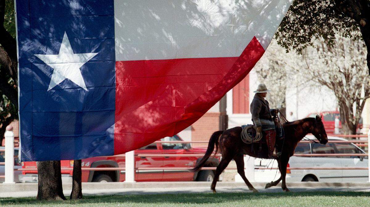 In this file photo from Texas Independence Day on March 2, 2002, a cowboy rides past a huge Texas flag in front of the Livestock Exchange Building at the Fort Worth Stockyards.