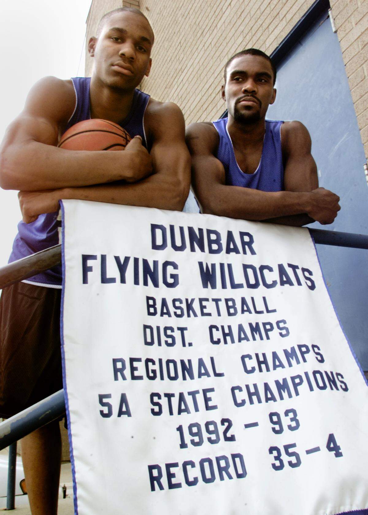 Jeremis Smith and Lance Jackson, members of the 2003 Dunbar High School basketball team stand over the 1992-93 5A State Championship banner.