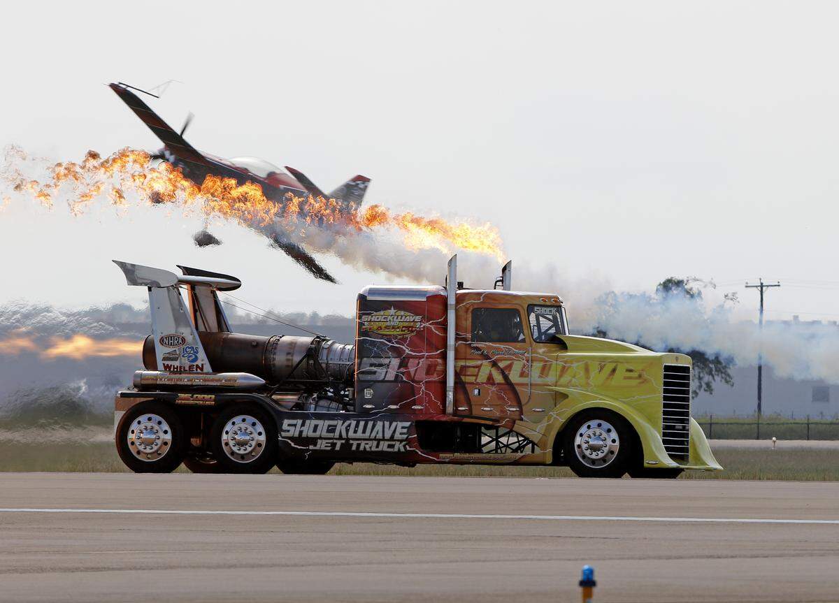 An aerobatic plane passes over the fiery, 3600 horsepower Shockwave Jet Truck during the Bell Fort Worth Alliance Air Show at Alliance Airport on Sunday in Fort Worth. Many modes of transportation, both civilian and military, were on display at the show, which was reduced to one day after bad weather canceled Saturday’s events.