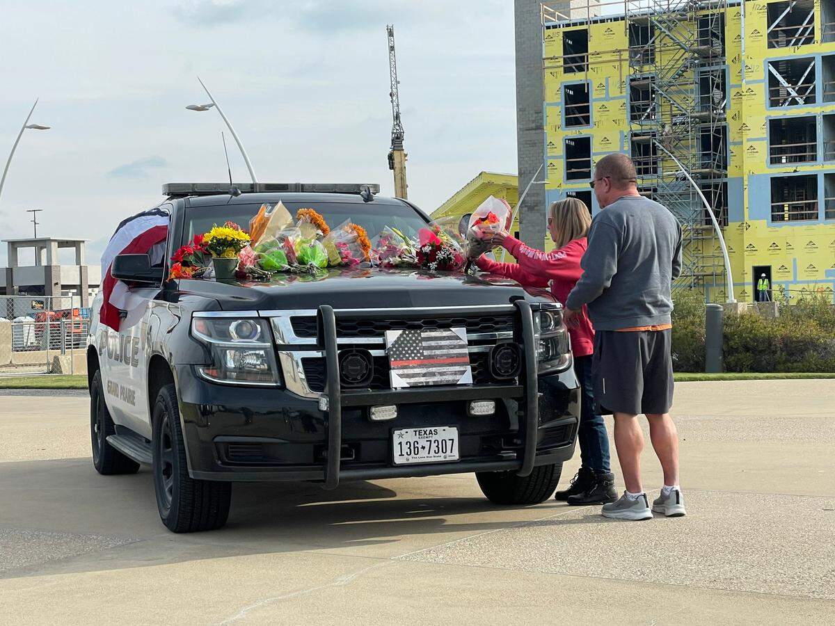 A woman places flowers on the hood of a Grand Prairie police vehicle designated as a memorial to an officer killed in a line-of-duty car crash Monday night.