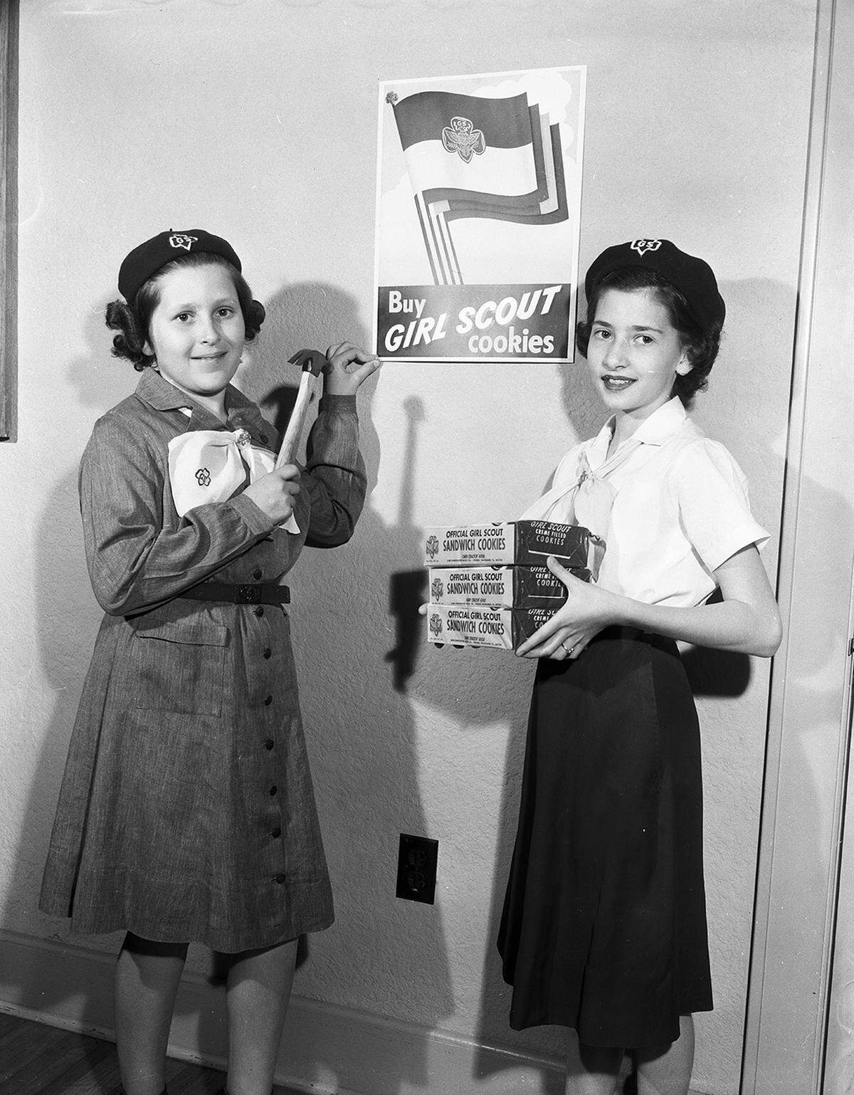 March 16, 1954: Fort Worth businesses are helping Tarrant County Girl Scouts sell cookies to raise money for Camp Timberlake, the Girl Scout camp on Eagle Mountain Lake, by displaying their posters. Barbara Sier, left, and Guthrie McRae, tack one up.